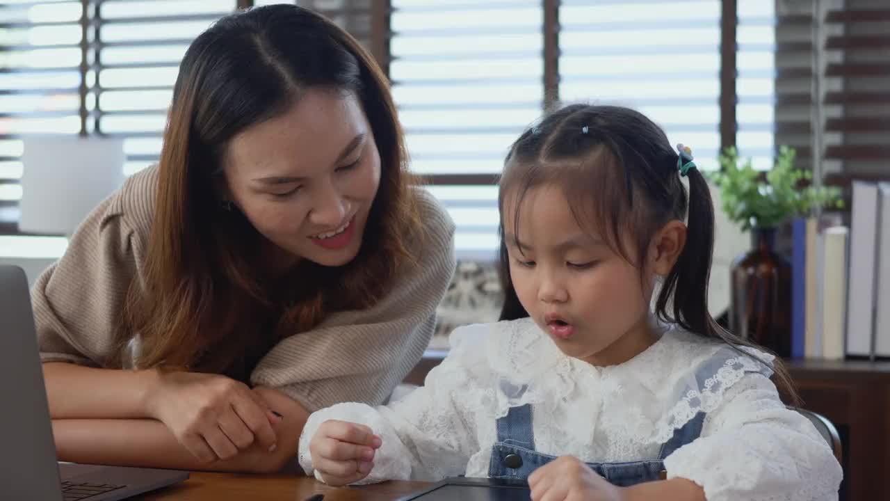 妈妈在家里用笔记本电脑工作，帮助女儿做作业视频素材