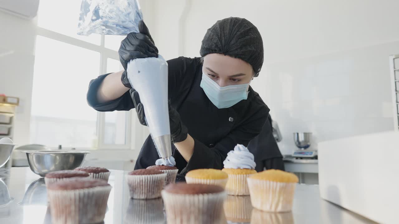 自信的专业糕点师用蓝色装饰松饼。在糖果店室内厨房工作的白人妇女戴着冠状病毒口罩的肖像。烹饪和工作。视频素材