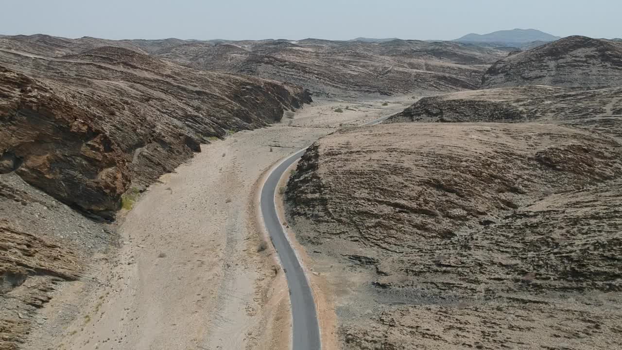 柏油马路蜿蜒穿越沙漠景观，道路两侧有石山高视点架空。视频素材