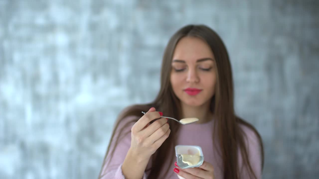 女人吃酸奶。4k年轻美女喝酸奶。正在节食吃酸奶的年轻女子。可爱，有吸引力的女人吃酸奶在白色浅灰色的背景视频素材