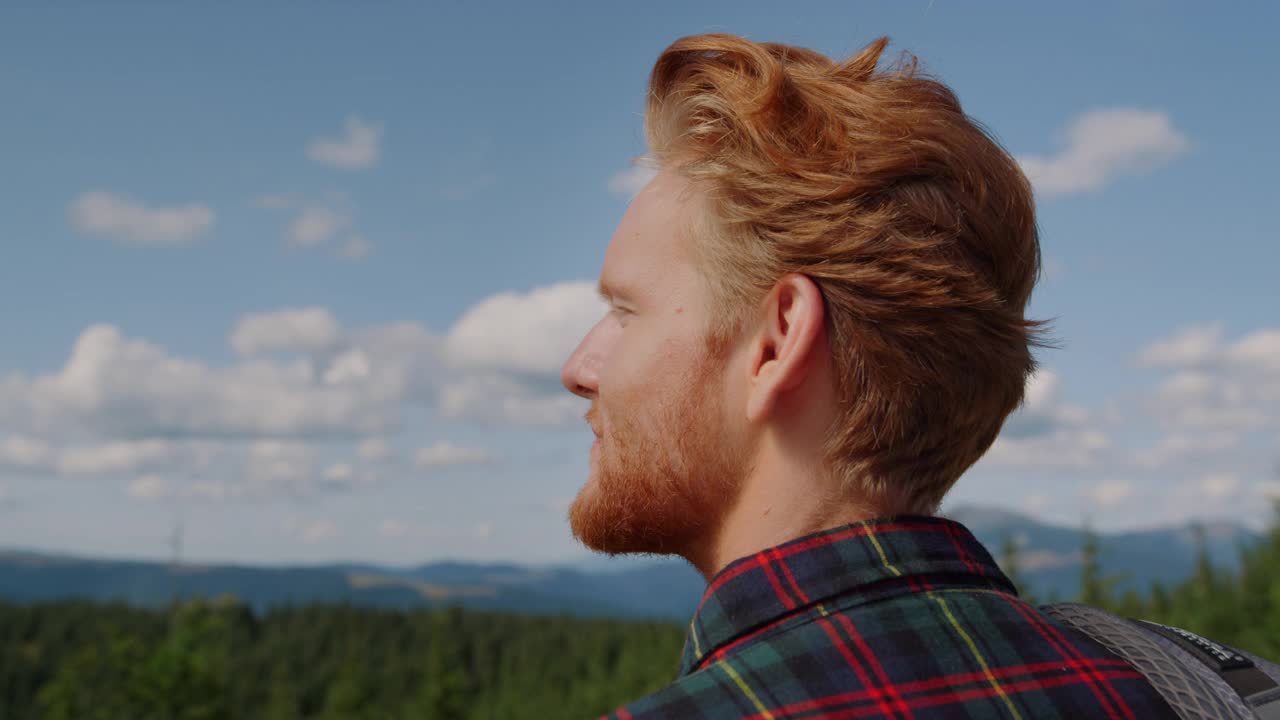 小伙子在夏天欣赏山景。男性旅行者看着绿色的树林视频素材