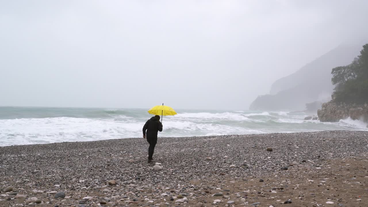 一个孤独的人在雨天走在海滩上视频素材