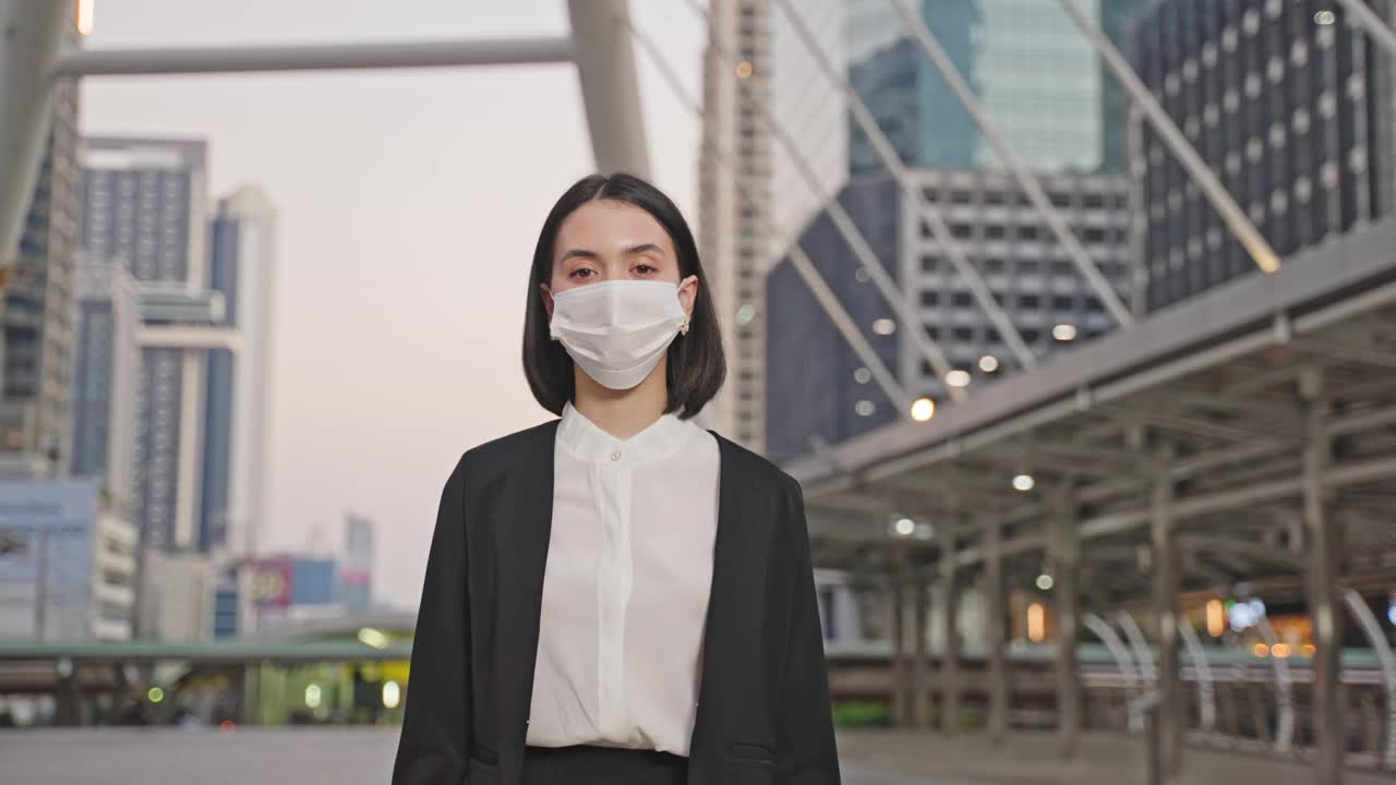 肖像亚洲年轻美丽的女商人站在户外与快乐和自信的脸在城市。聪明的工作妇女脱下或戴上防护口罩，以防止感染新冠病毒。视频素材