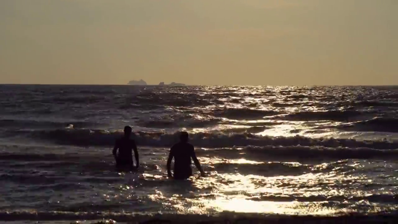 人们在日落、日出时在大浪中沐浴，而在波涛汹涌的海面上站在浅水中视频素材