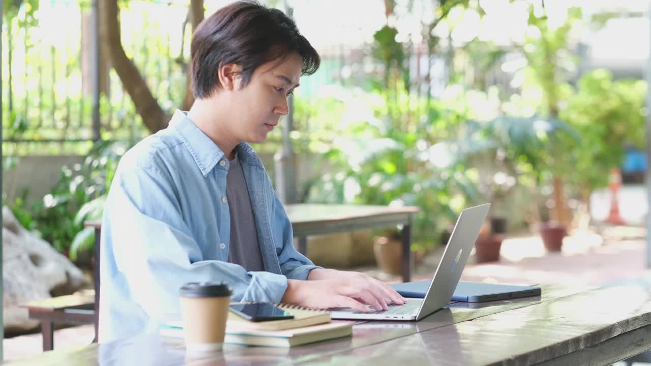 年轻的亚洲大学男子在校园里通过笔记本电脑边讲电话边在线学习，网络教育理念视频素材