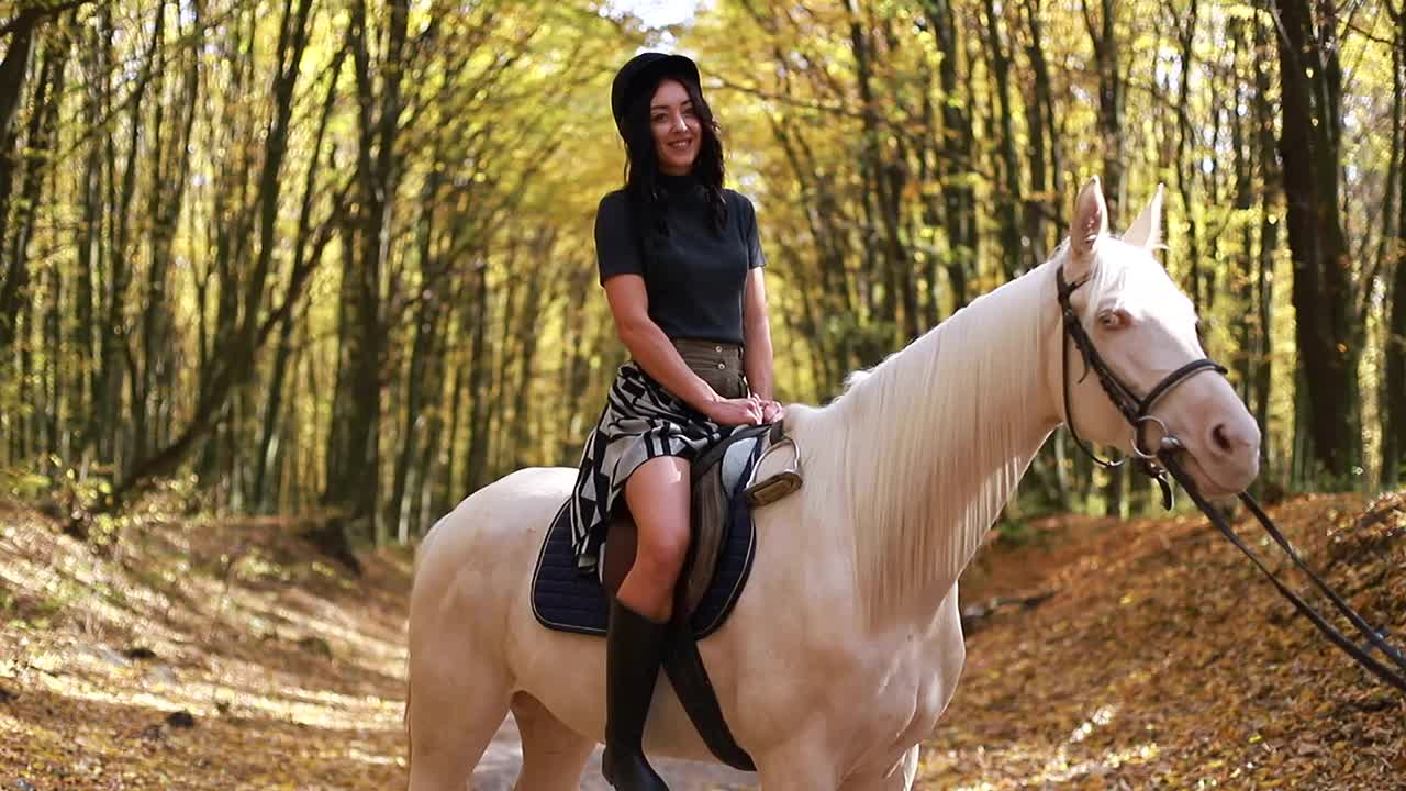 一个年轻的女孩在树林里骑着一匹白马。骑视频素材