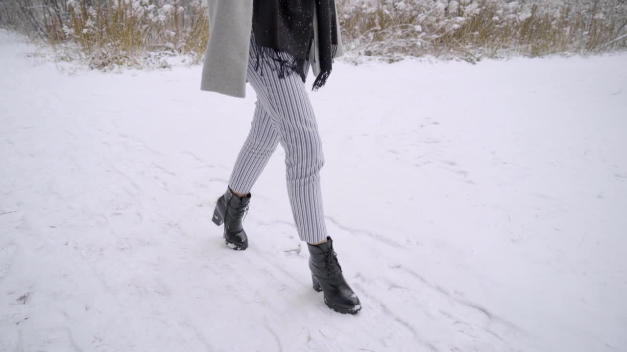 一个年轻漂亮的女人在雪地里用手机打电话，她正在室外的一个冬季公园里散步。缓慢的运动。年轻漂亮的女人在冬天的公园里打电话。女性使用智能手机视频素材