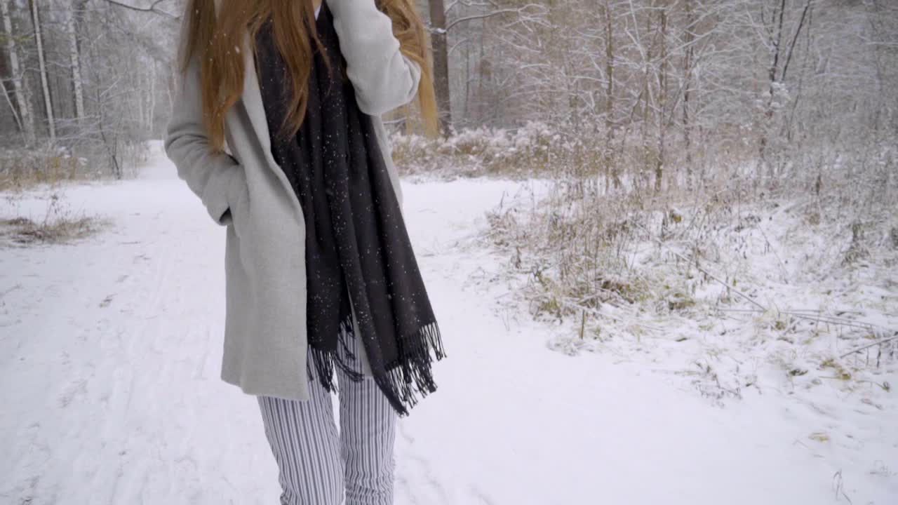 一个年轻漂亮的女人在雪地里用手机打电话，她正在室外的一个冬季公园里散步。缓慢的运动。年轻漂亮的女人在冬天的公园里打电话。女性使用智能手机视频素材