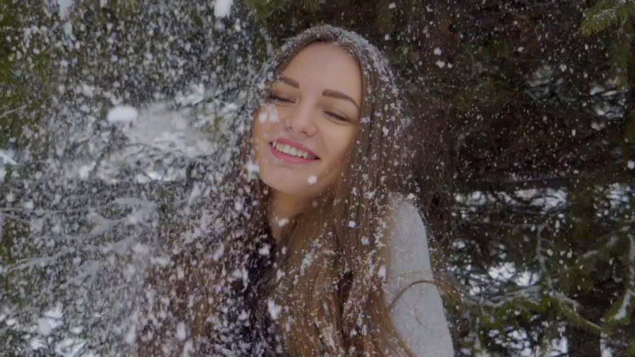 雪花飘落在美丽女孩的脸上和长发上。白雪背景下年轻美丽的女人的肖像。雪花落在她的头发上。缓慢的运动。它正在下雪。在户外。她在冬天很快乐。面带微笑。冬天的公园。冬季森林视频素材