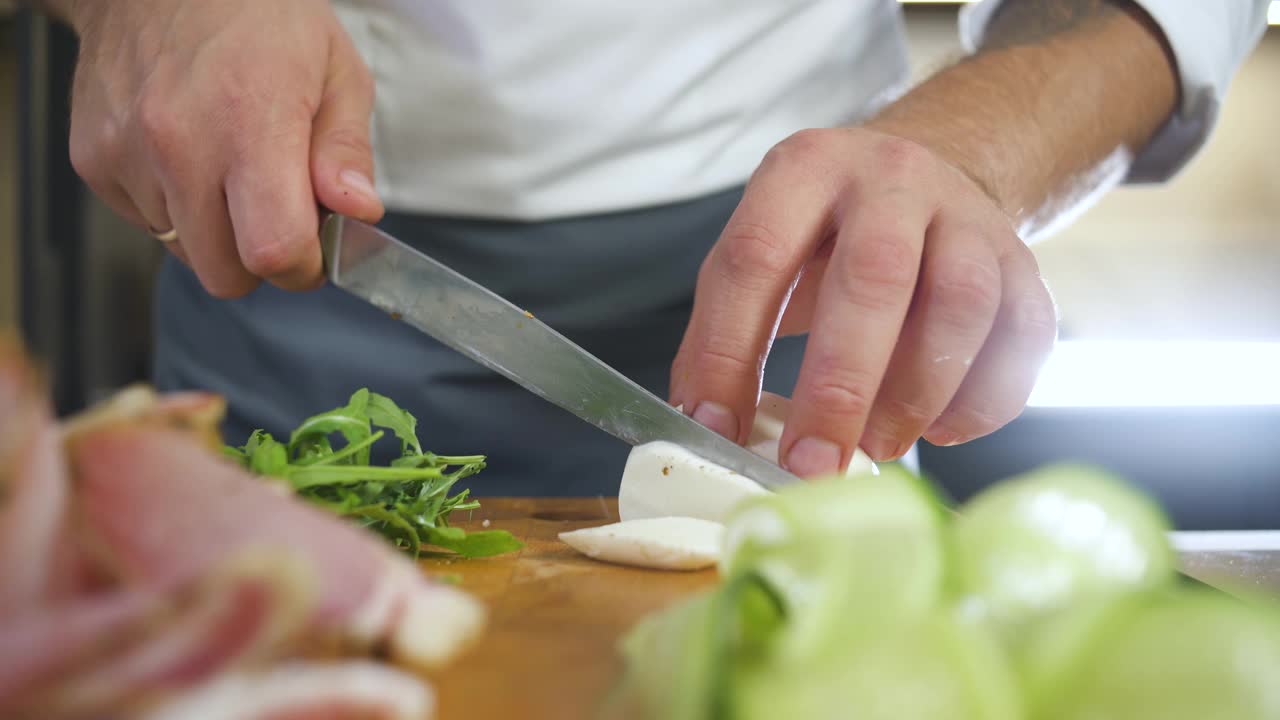 专业厨师在餐厅厨房用刀切马苏里拉芝士。男人为准备素食健康食物而切蔬菜。在厨房里做美味的菜。视频素材