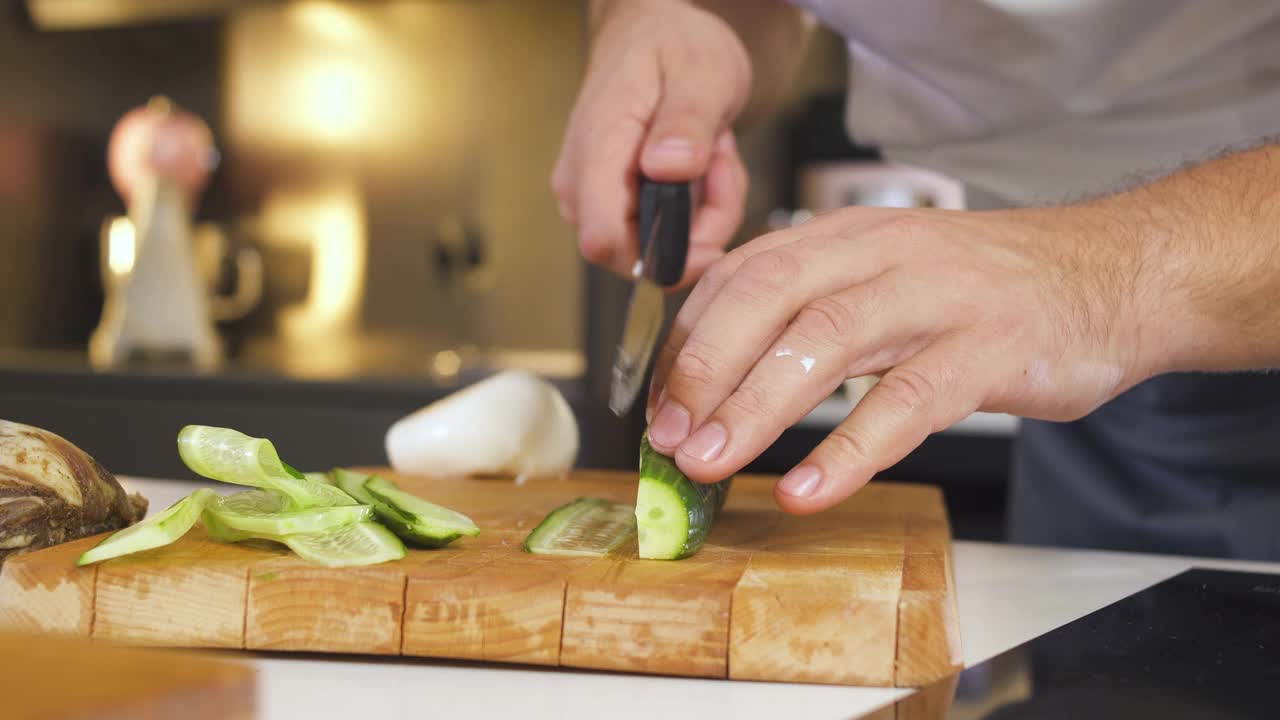 专业厨师在餐厅厨房砧板上用刀切黄瓜。男人为准备素食健康食物而切蔬菜。在厨房烹饪美味的节日菜肴。视频素材