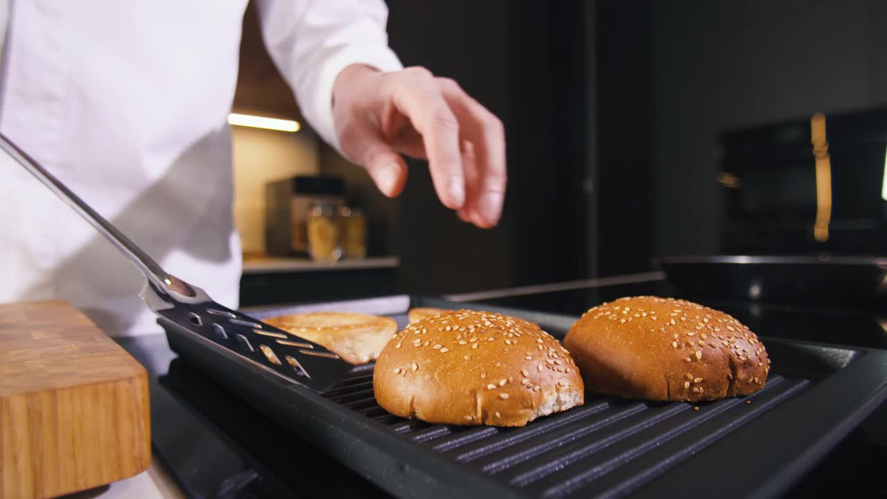 Man Fries Burger Buns In Grill Pan为家庭现代厨房做美味的汉堡晚餐。厨师在餐厅烹饪食物。在厨房准备饭菜。美味快餐菜肴特写视频素材