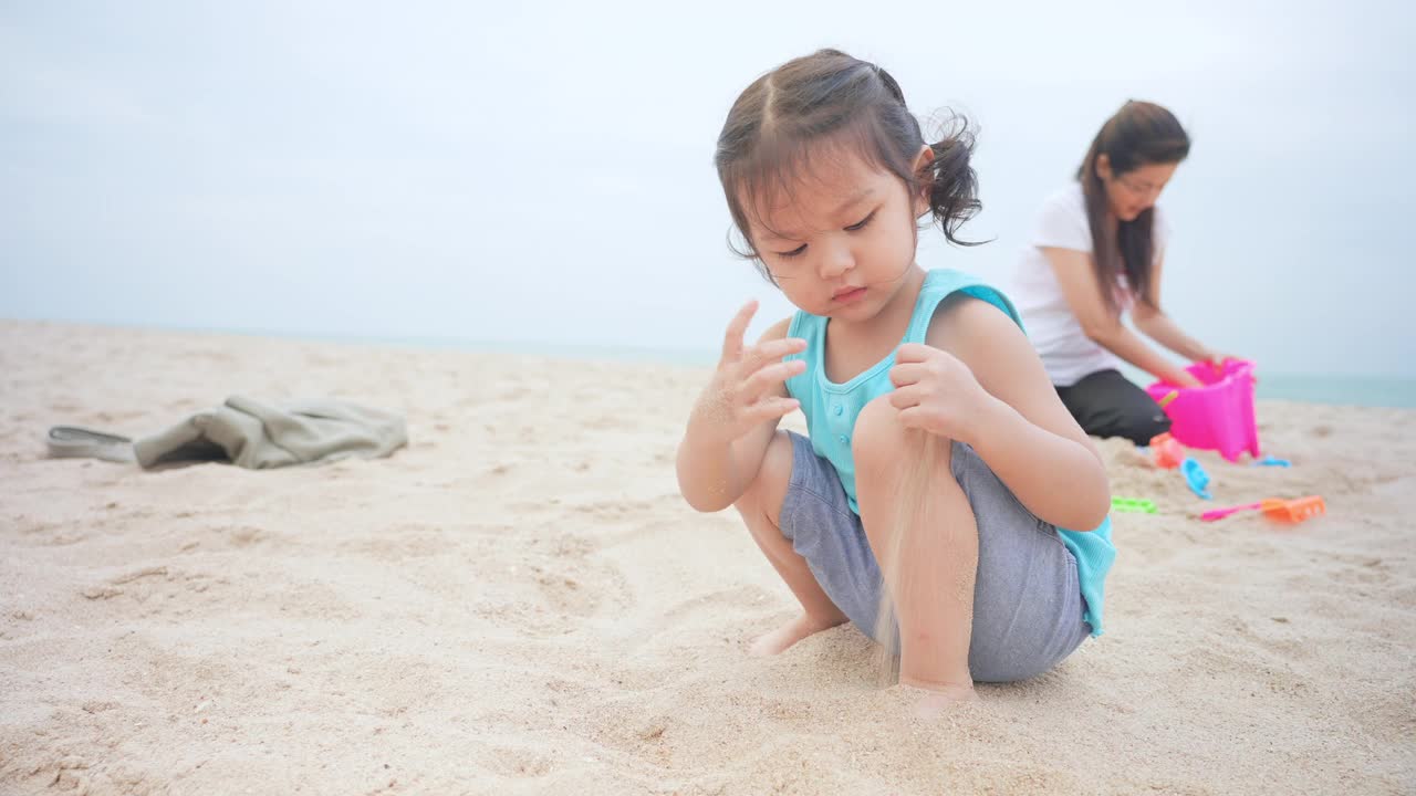 近距离观看女儿和母亲在沙滩上玩沙堡在暑假时间。视频素材