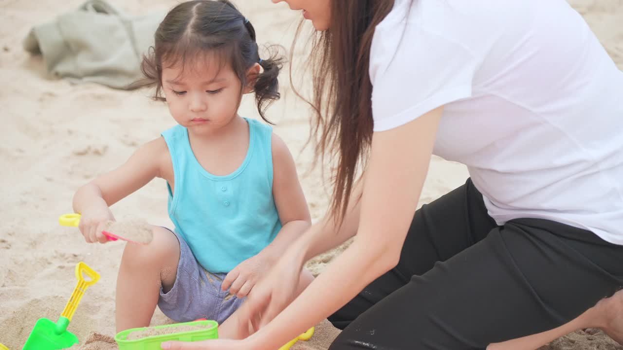 近距离观看女儿和母亲在沙滩上玩沙堡在暑假时间。视频素材