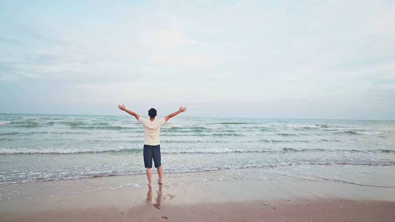 亚洲男人在海滩上散步，举起手来放松自己视频素材