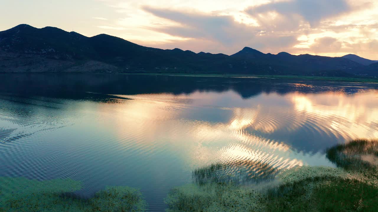 美丽的日落天空倒映在黑山的斯卡达尔湖。前景是沼泽草，远处群山的剪影。视频素材