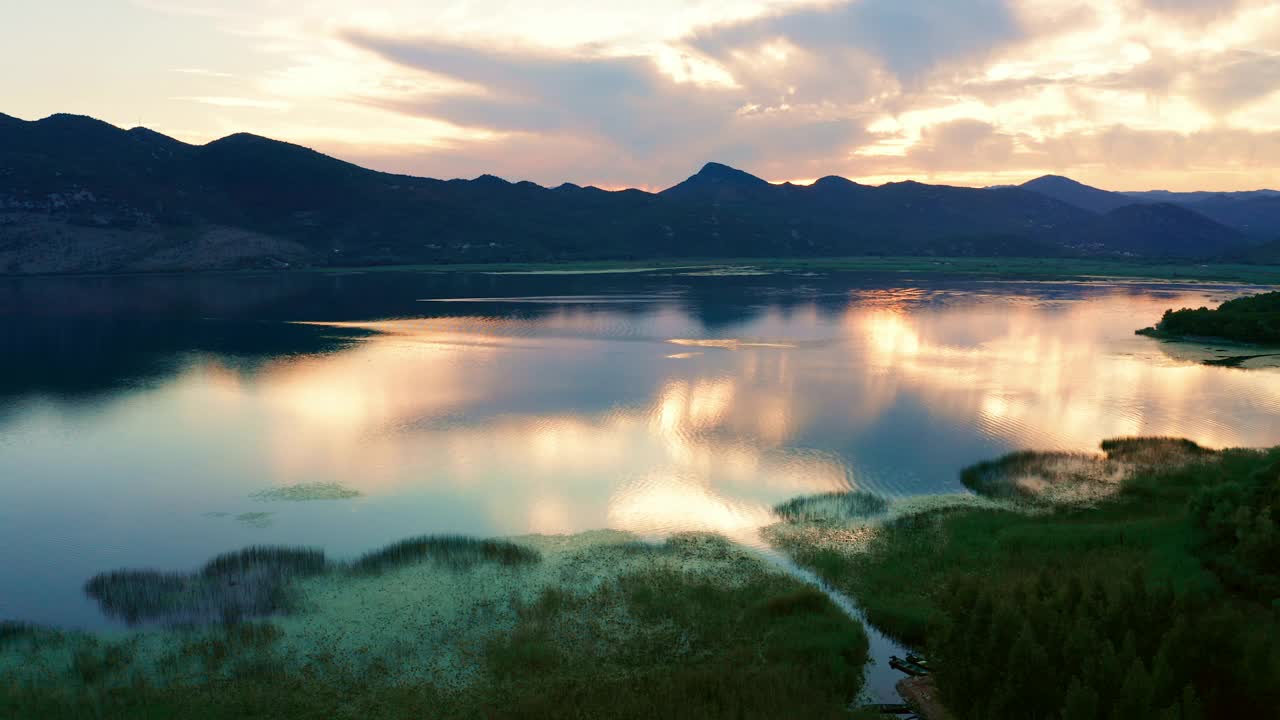 美丽的日落天空倒映在黑山的斯卡达尔湖。前景是沼泽草，远处群山的剪影。视频下载