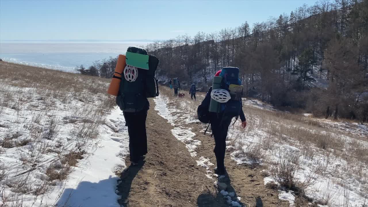 一群背着背包的游客沿着小路走向结冰的贝加尔湖。视频素材