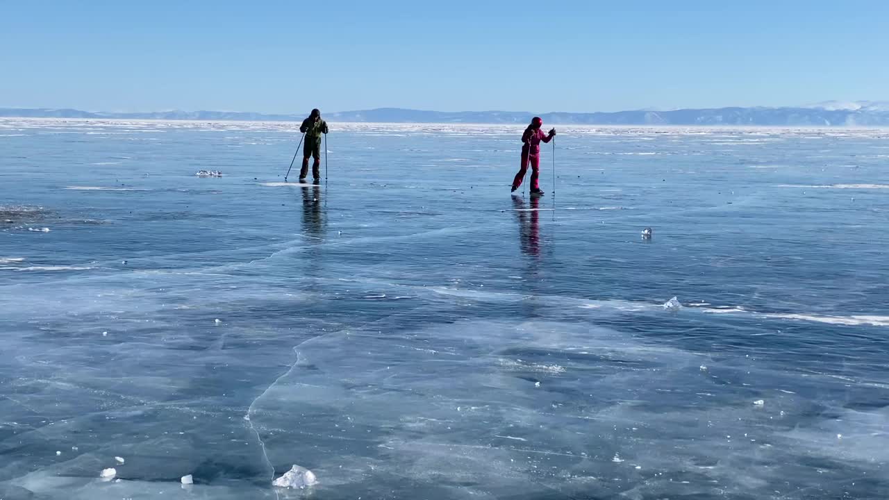 在贝加尔湖上滑冰。一个男孩和一个女孩拿着滑雪杖在结冰的贝加尔湖上滑冰。视频素材