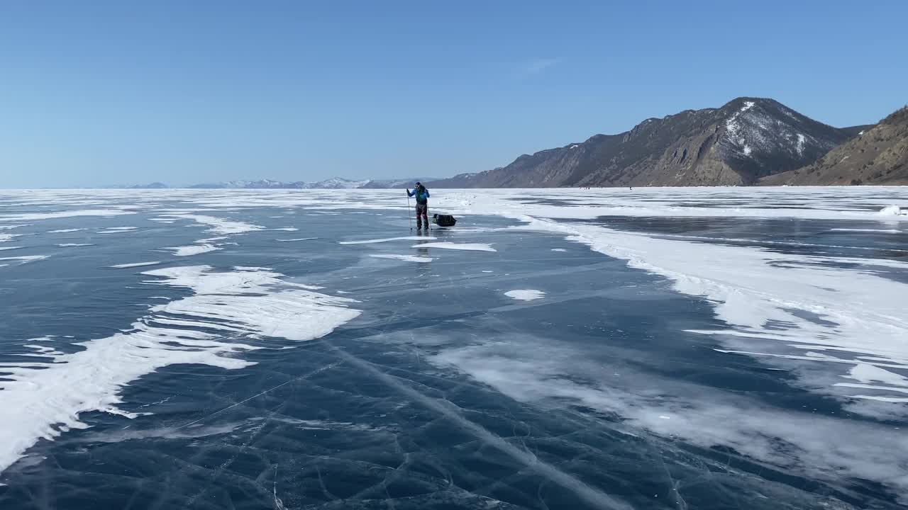 一个戴着头盔、穿着溜冰鞋、带着护膝、带着滑雪杖、背着背包的家伙正在贝加尔湖的冰面上打滚。视频素材