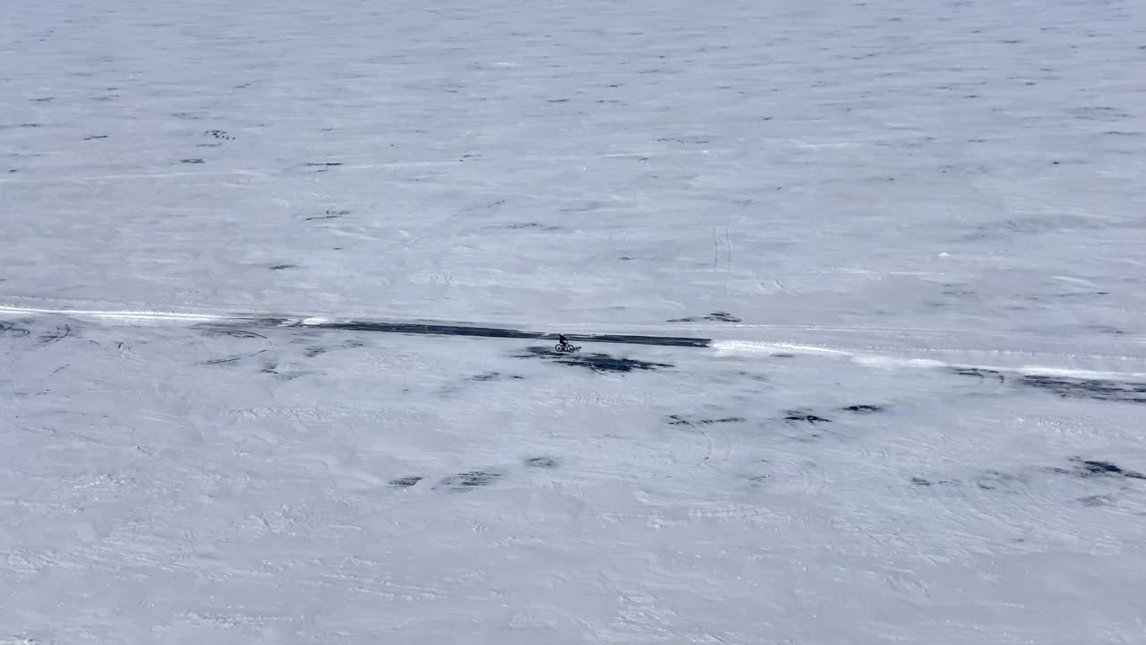 一名骑自行车的人沿着冰雪覆盖的贝加尔湖骑行。远景，俯视图。视频素材