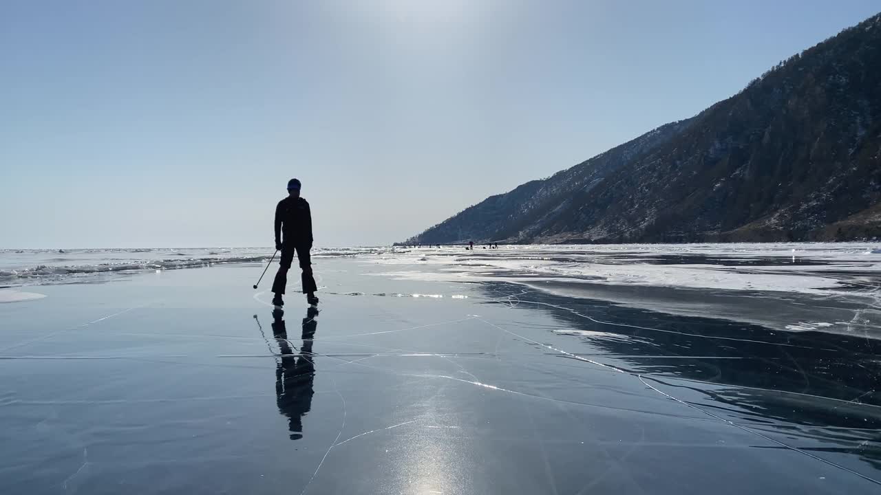 一个戴着头盔、穿着溜冰鞋、拿着滑雪杖的年轻人正在结冰的贝加尔湖上滑冰。视频素材