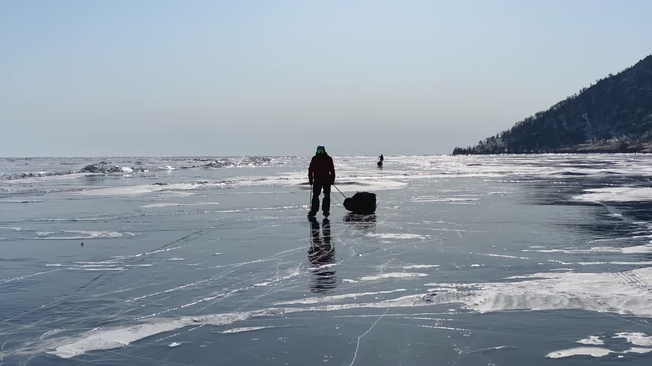 两名游客穿着溜冰鞋，手持滑雪杖，在贝加尔湖的冰面上滑行。视频素材