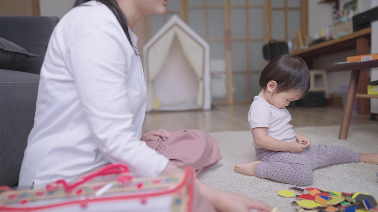 抓拍年轻的黑发妈妈帮她的女儿玩彩色拼图，顽皮的小女孩正在选择拼图填补棋盘游戏的空白，母亲在玩时间视频素材