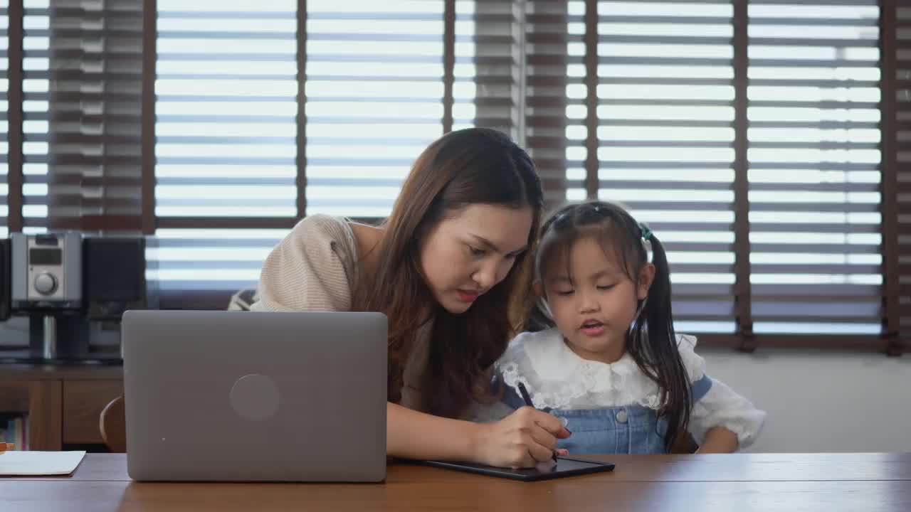 妈妈在家里用笔记本电脑工作，帮助女儿做作业视频素材