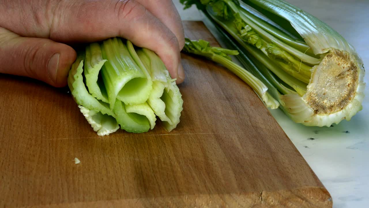 厨师用菜刀将芹菜茎切成小片放在厨房木板上做蔬菜沙拉。视频素材