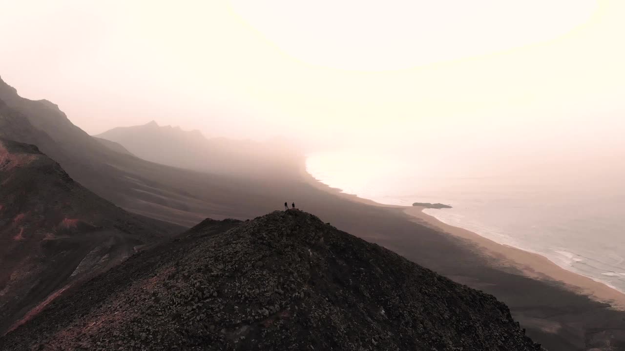 无人机拍摄的两名男子从火山景观的视角俯瞰富埃特文图拉的野生海岸。西班牙。视频素材