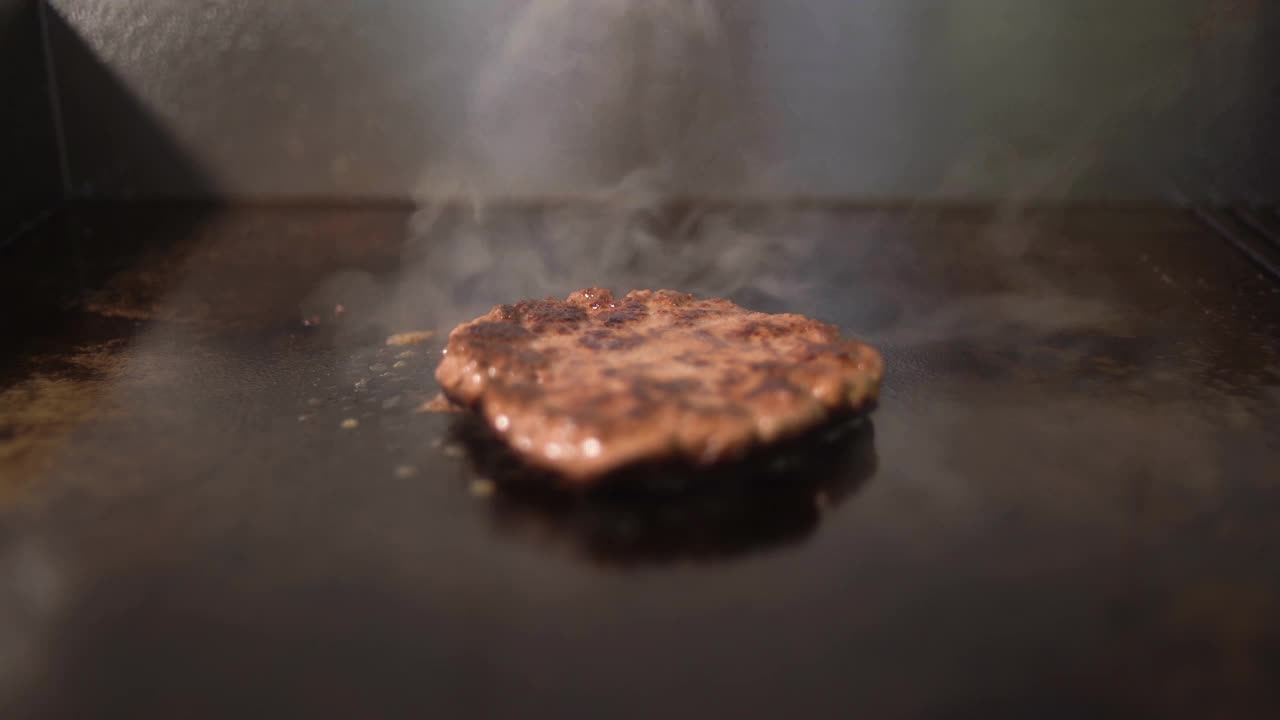 做一个芝士汉堡的牛肉和猪排。肉在厨房里烤。多汁的肉用抹刀压扁。视频素材