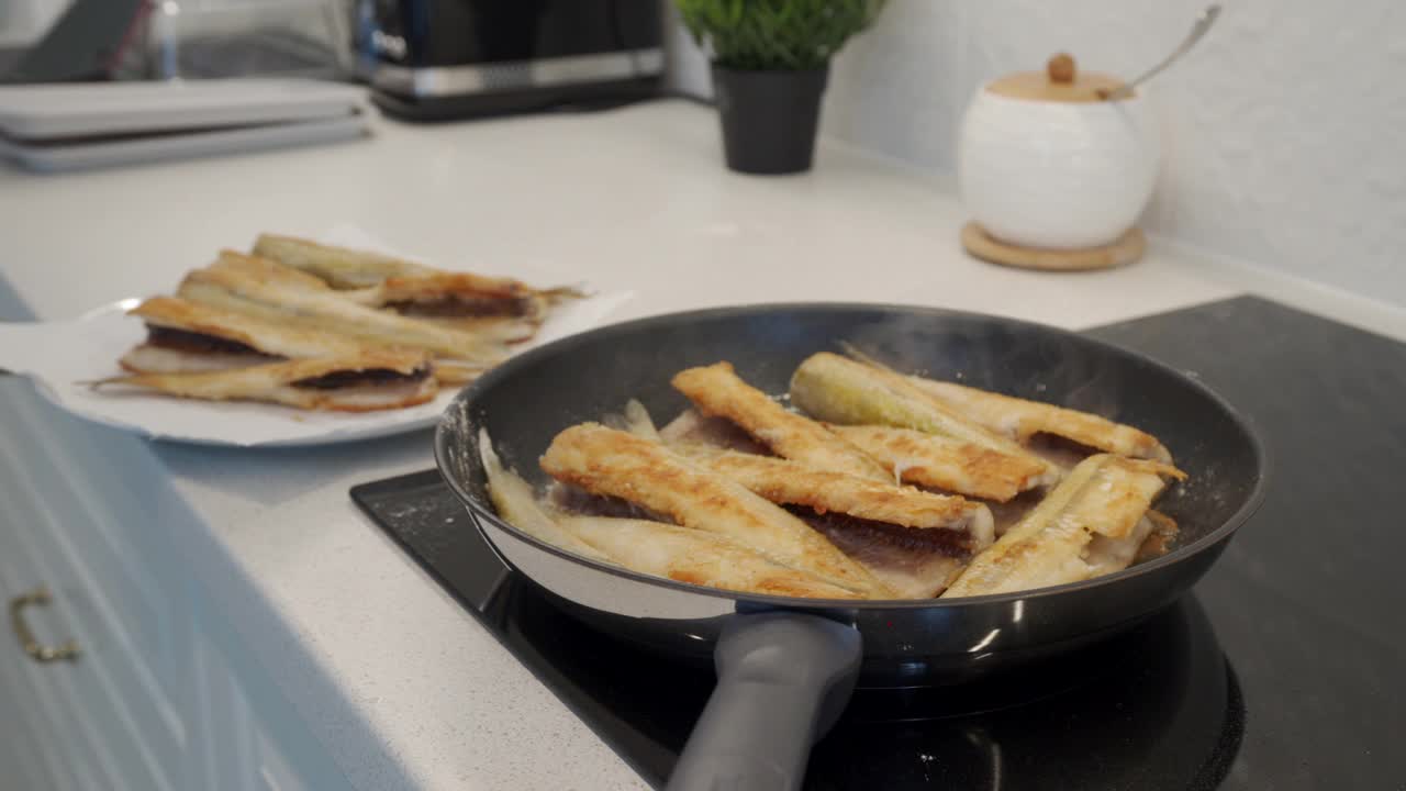 在现代的白色厨房里烹饪晚餐，鱼香在煎锅里炸。视频素材