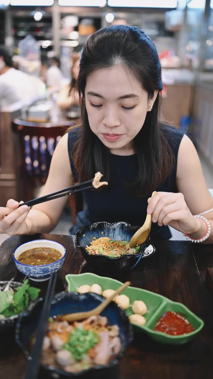 年轻的亚洲妇女正在吃泰国式午餐面条，新鲜的汤从一个用木筷子被称为“船面”的碗里视频素材