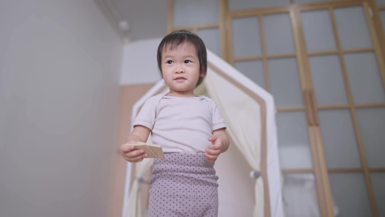 健康可爱的亚洲女婴在家里学习如何站立和走路，人类生长科学保健，天真的幼童看着相机，舒适的家庭背景简单的生活视频素材