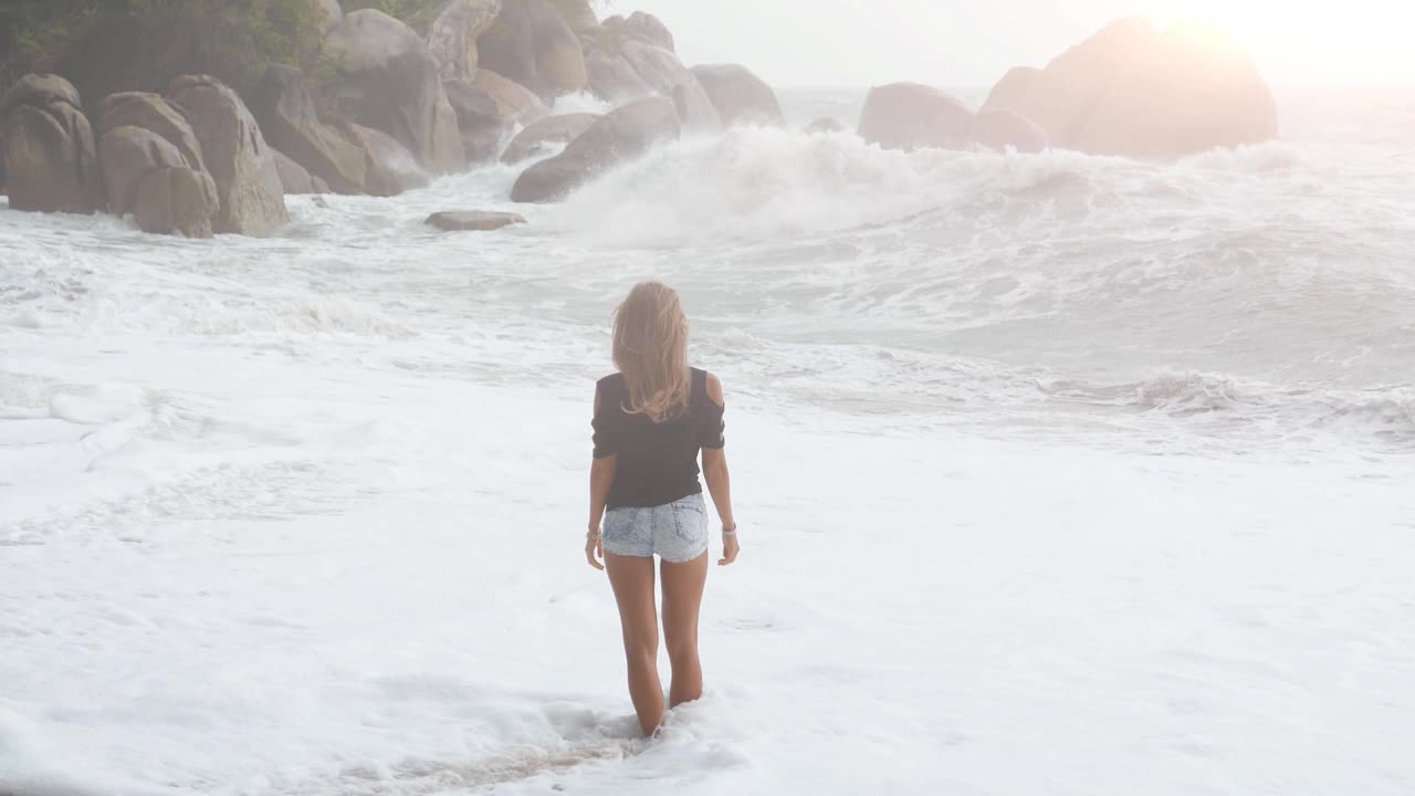 海滩上的时尚女人。年轻女子站在暴风雨中的海滩上。视频素材