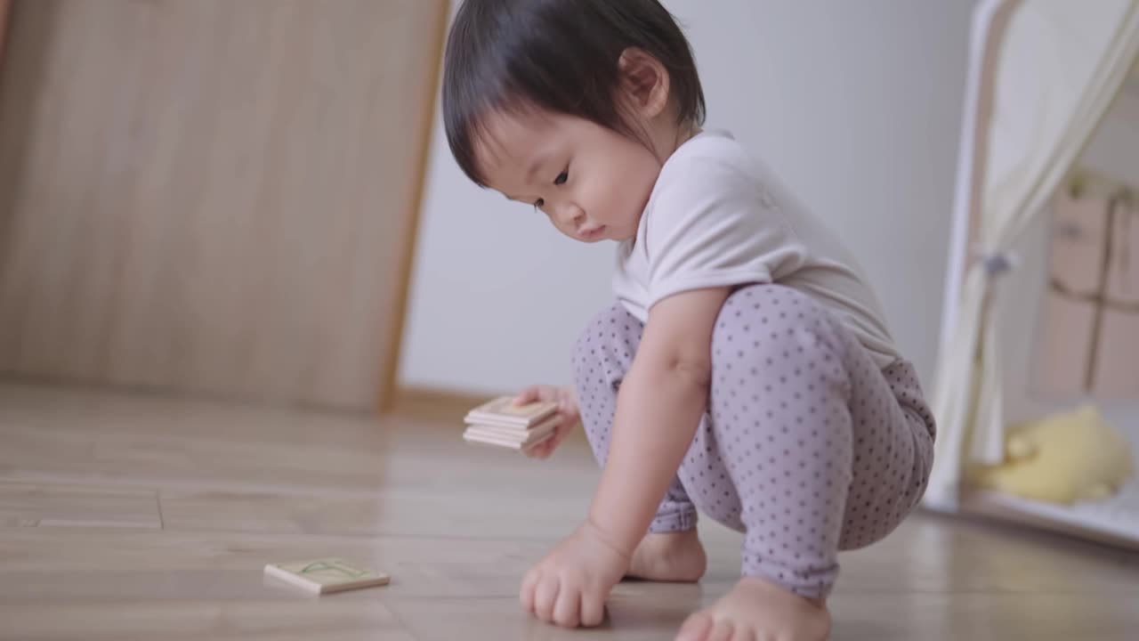 在家里的一天，帮助妈妈打扫房间，可爱的小女孩在客厅的木地板上收集她自己的玩具，周末上幼儿园，孩子安全地呆在家里视频素材