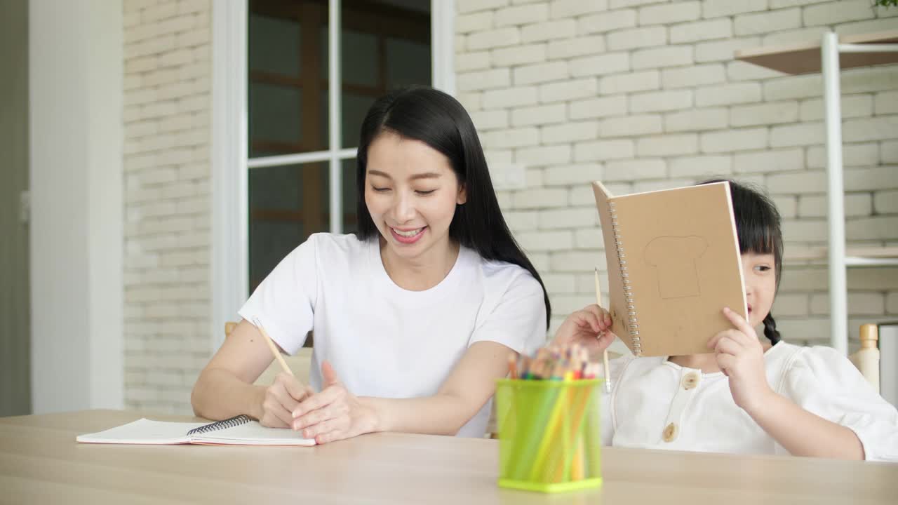 年轻的母亲教女儿在家做作业视频素材