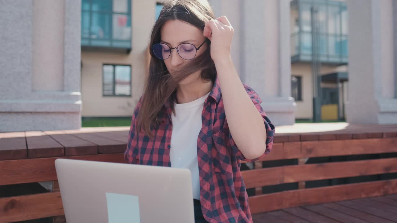 一个女孩在公园里远程工作的照片。穿着格子衬衫的年轻商业女性，在笔记本电脑上做笔记的自由撰稿人视频素材