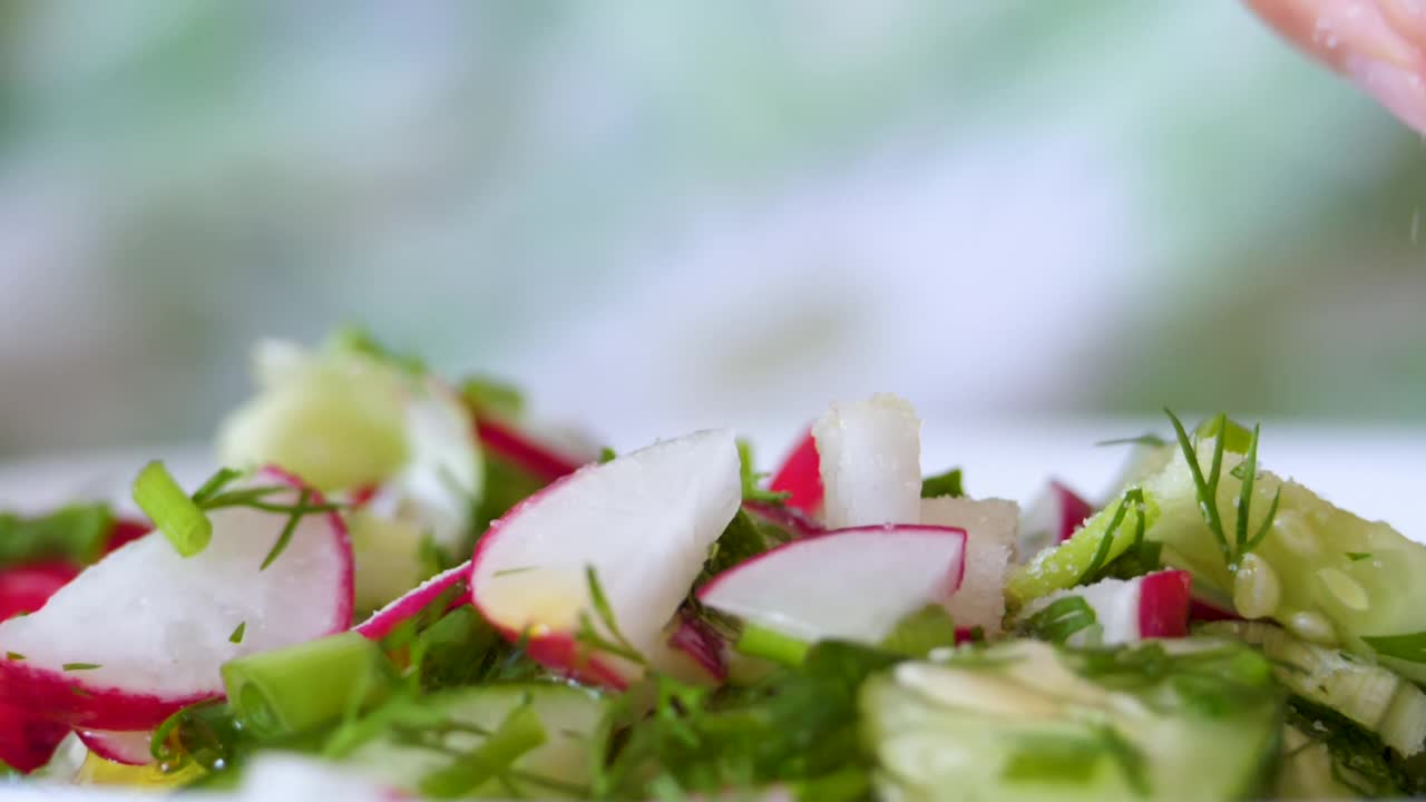 厨师洒白盐蔬菜新鲜沙拉食物健康餐地中海厨房素食饮食。缓慢的运动。特写镜头新鲜沙拉。近距离观察健康多彩的食物洋葱、黄瓜、萝卜。视频素材