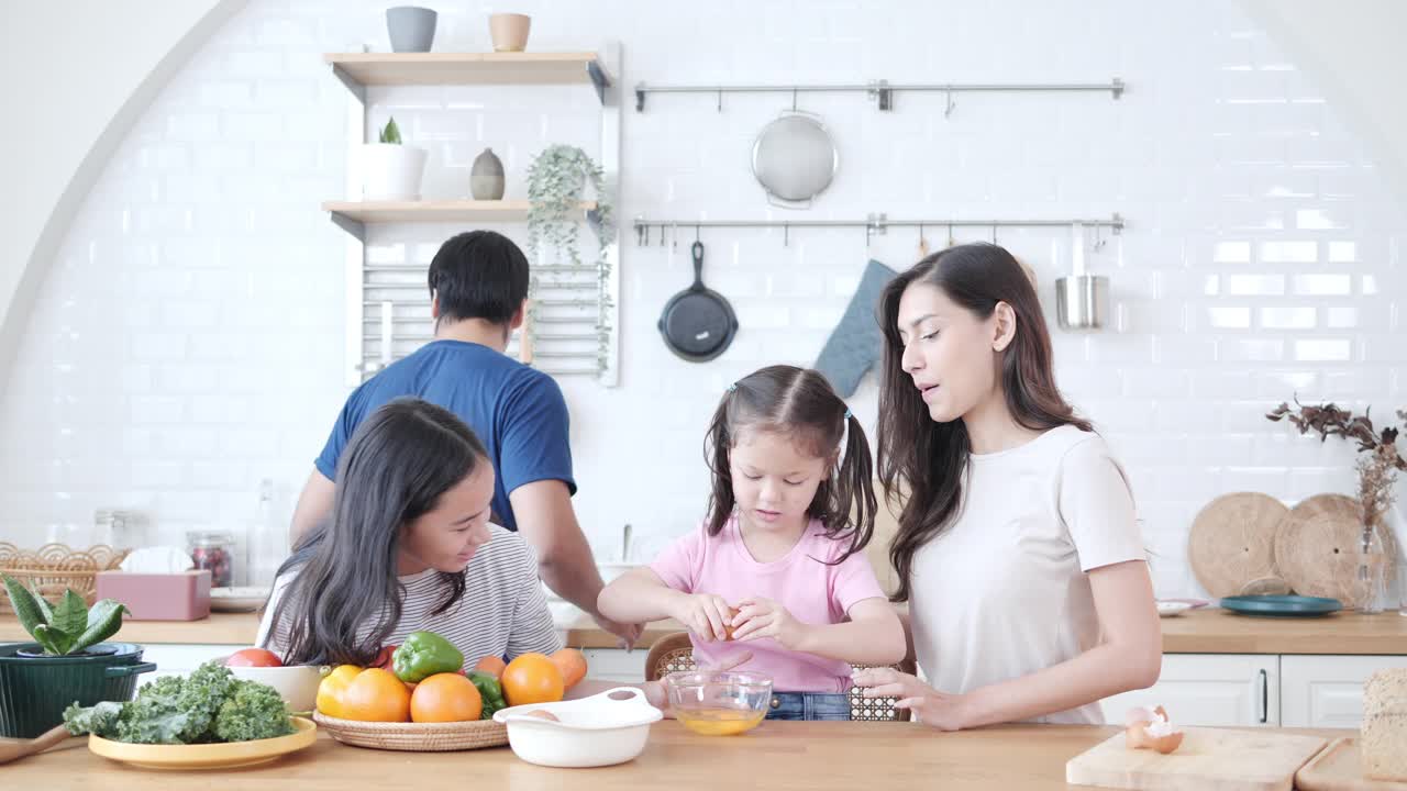 幸福的跨种族夫妇在现代厨房里教混血女儿们准备新鲜健康的食物。微笑的多种族家庭参与烹饪和可爱的孩子。视频素材