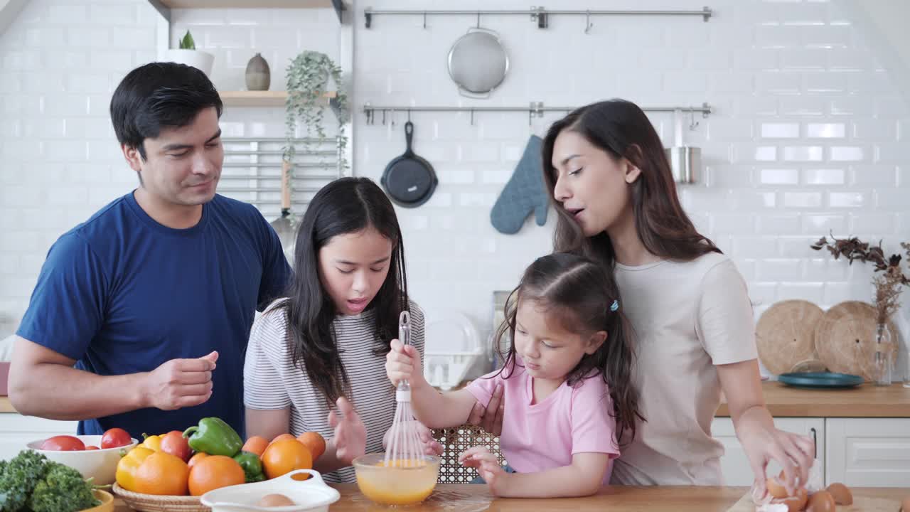 幸福的跨种族夫妇在现代厨房里教混血女儿们准备新鲜健康的食物。微笑的多种族家庭参与烹饪和可爱的孩子。视频素材