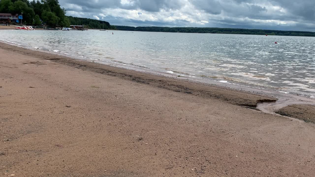 在夏天的阴天里，一个湖的沙质河岸，清澈的水和小波浪视频素材