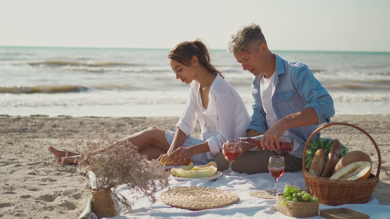 男人往玻璃杯里倒酒，女人切瓜。快乐的人们在海上度假，浪漫的旅行视频素材