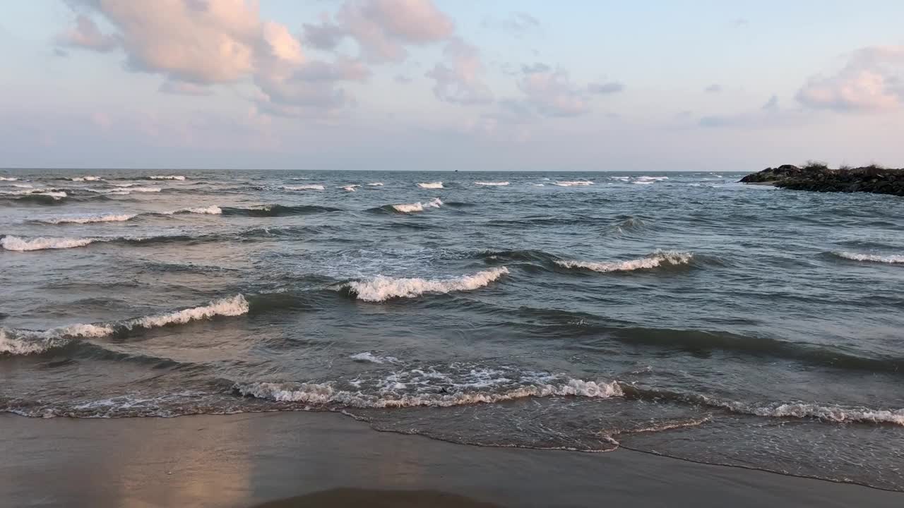 夏季傍晚日落时，海浪在海岸海岸线上流动。在夏日黄昏的黄金时刻，海滩的波浪不断地流动。视频下载