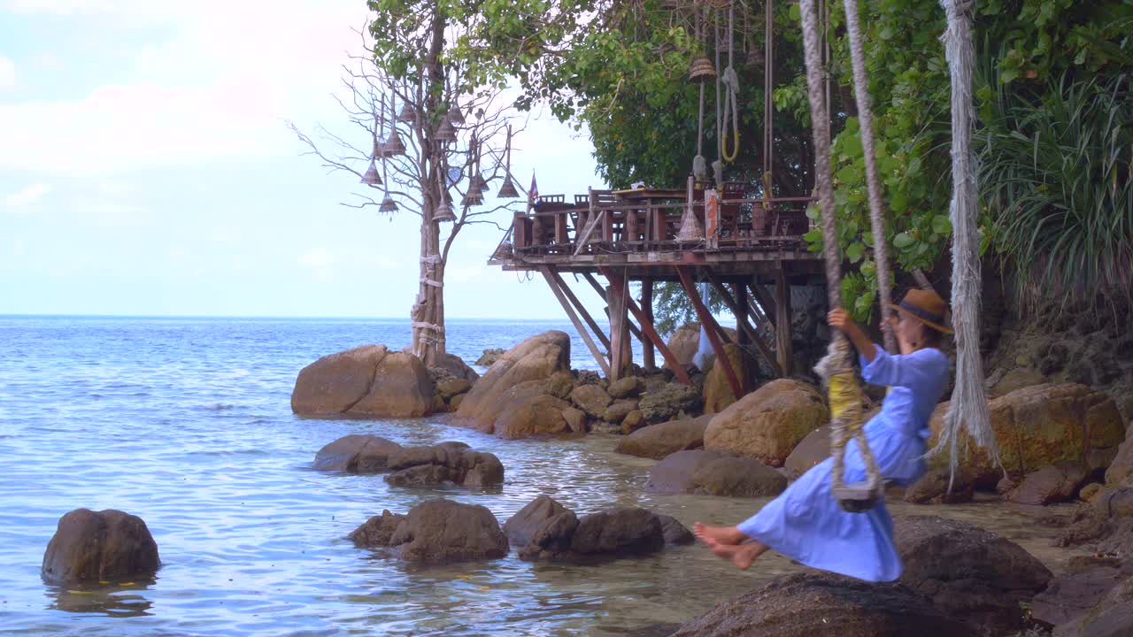 美丽的女人坐在秋千上，美丽的浪花拍打着海里的石头视频素材