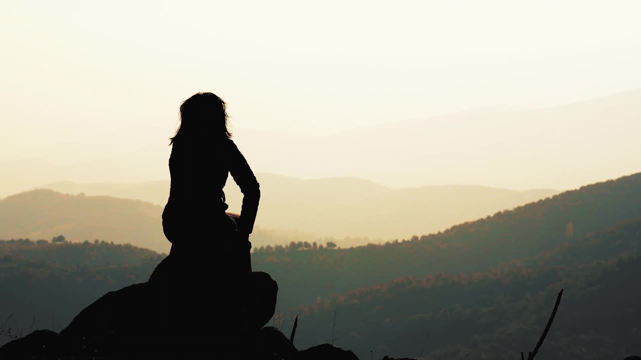 年轻女子坐在山顶和美丽的山在雾日落在夏天视频素材