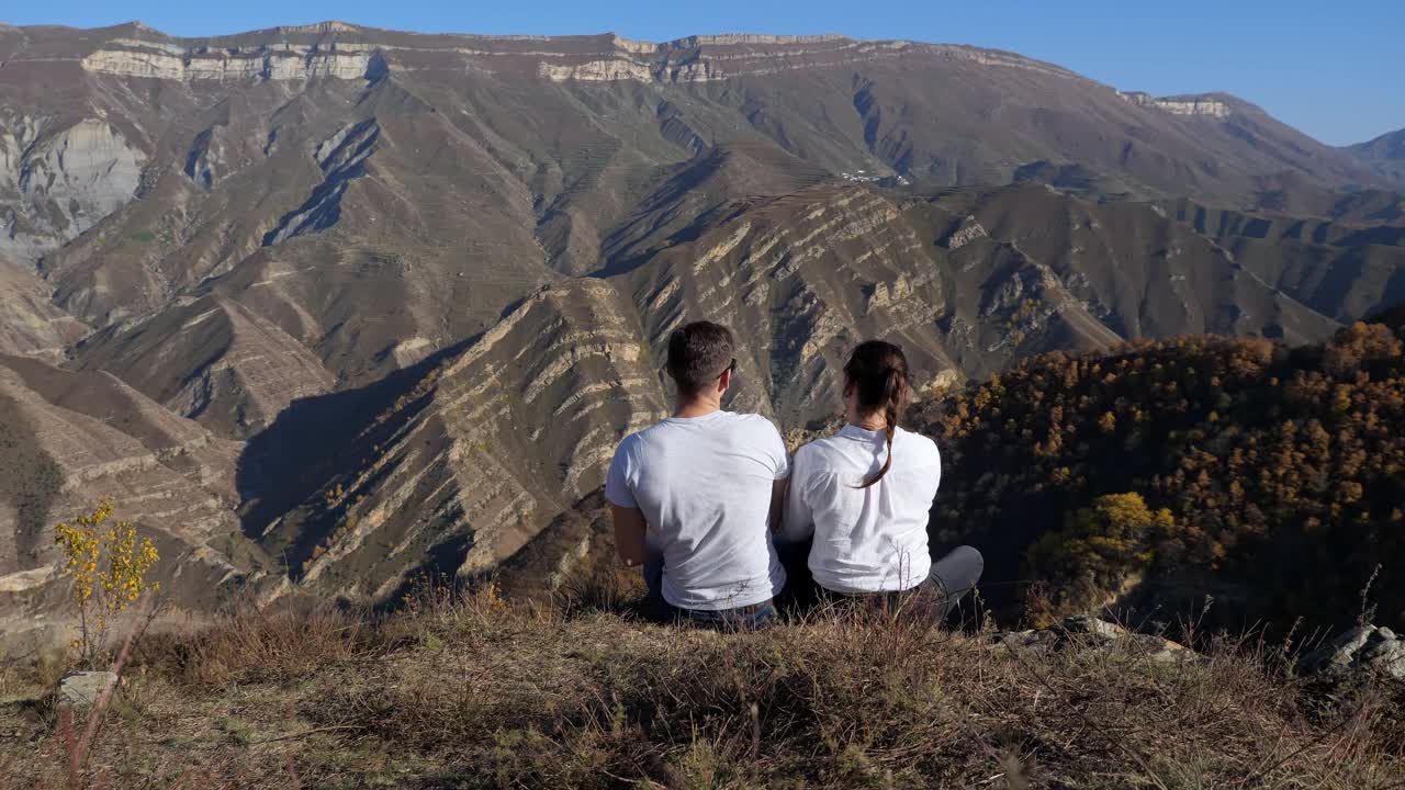 一对男人和女人坐在山坡上，看着山谷，背景视频素材