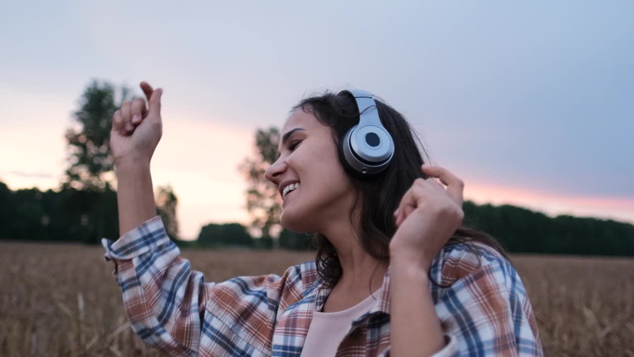 一个年轻女子的肖像与耳机听音乐，唱歌和有趣的舞蹈在自然界视频素材