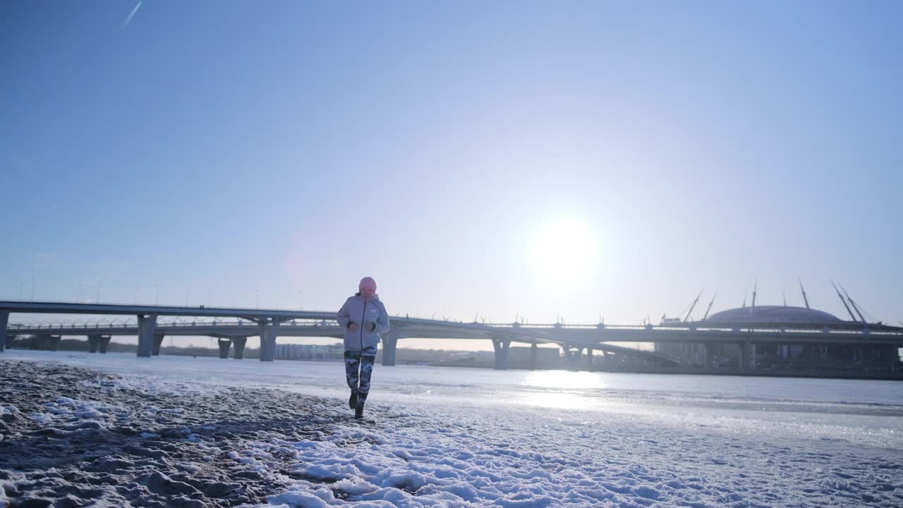 女孩在冬天沿着白雪覆盖的沙滩跑步视频素材